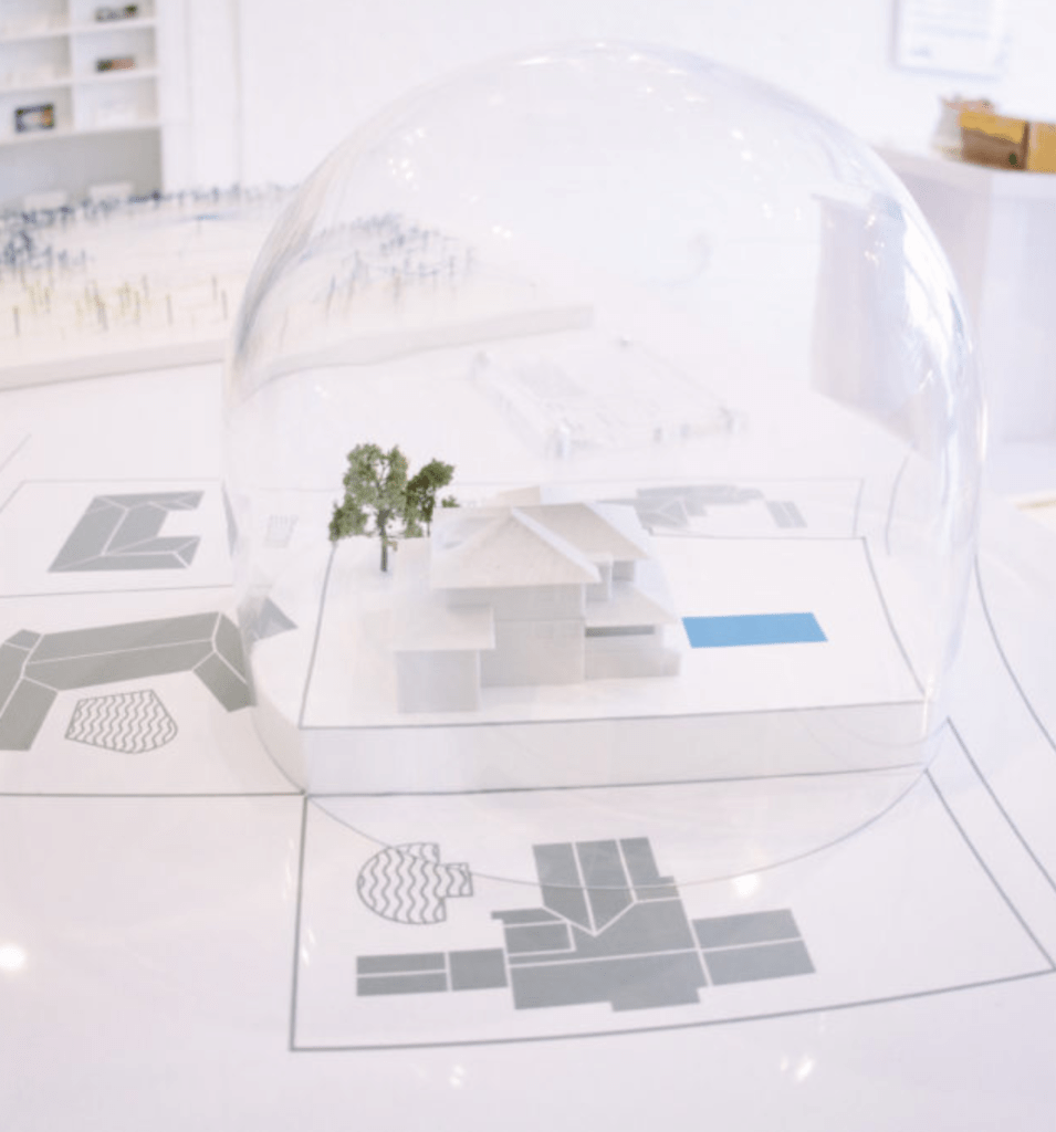 반구형의 투명한 유리 안에 바닥보다 약간 높은 지지대가 꼭 맞게 사각형으로 들어가 있고, 그 위에 3d 프린팅으로 만든 집이 있고, 그 옆에 플라스틱 나무가 두 그루 서 있다. 집 옆으로는 파란색 사각형이 있다. 반구형 안팎은 바닥으로 연결되어있고 반구형 주변으로는 네 개의 집의 도면이 회색으로 바닥에 그려져 있다.